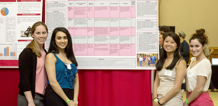 Four students smiling in front of their research poster containing a large table and much data