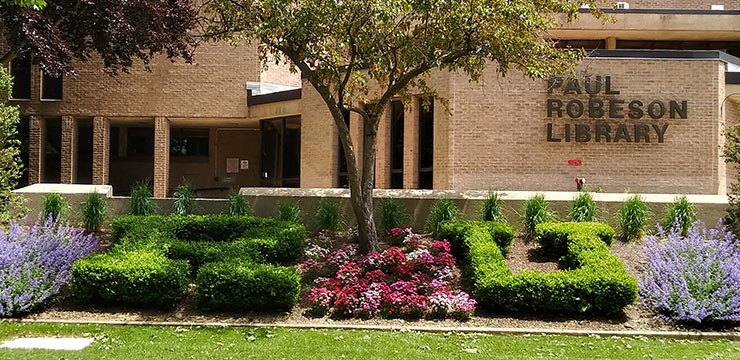 External photo of Paul Robeson Library entrance in Spring. Bushes outside the entrance are carved into the letters "R" and "U."