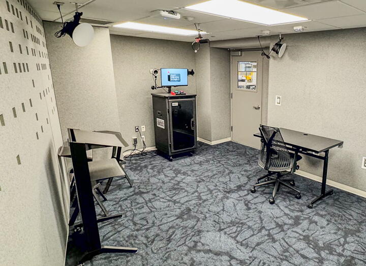 Interior of AV recording studio. Room includes soundproofing, podium, cameras, lighting, monitor, and big red and green buttons.