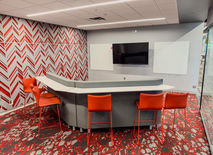 Group collaboration space with bar stool type seating and wall-mounted digital display and whiteboards