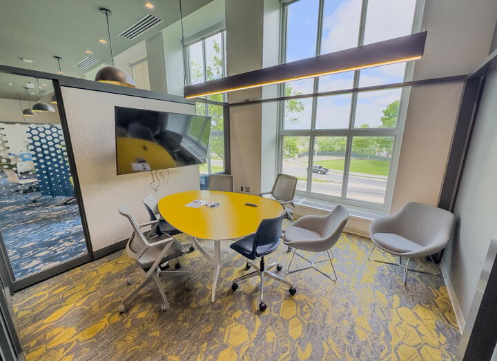 Interior of group study room with yellow table, gray chairs, a large, wall-mounted display, and a wall of windows