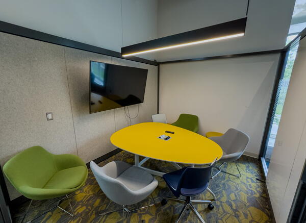 Interior of group study room with egg-shaped yellow table, green and gray chairs, and a wall-mounted display