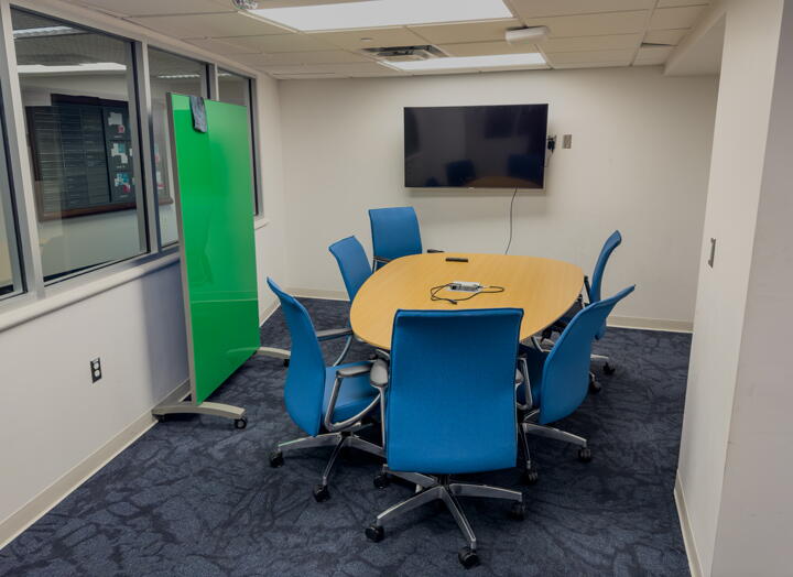 Interior of group study room with a large table, chairs, a wall-mounted display, and a whiteboard