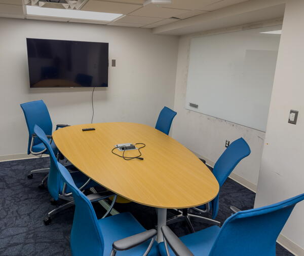 Interior of group study room with a large table, chairs, a wall-mounted display, and a whiteboard