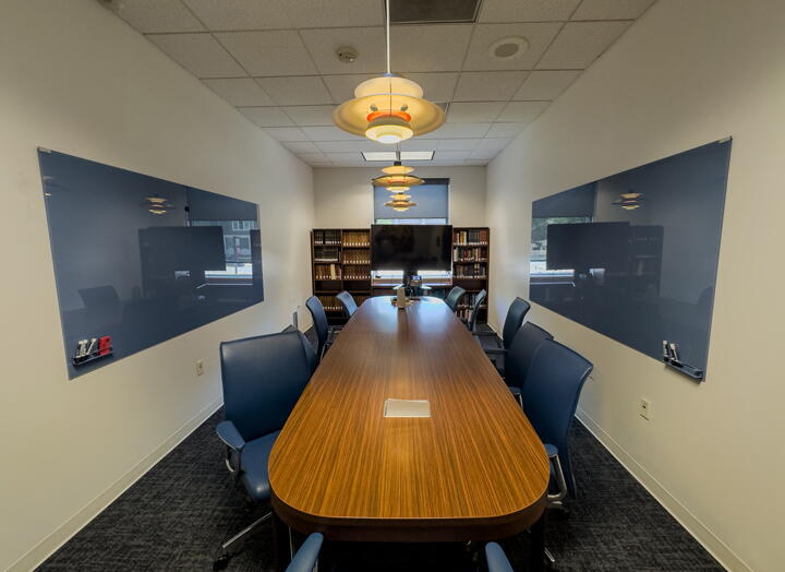 Conference room with long, wood conference table and chairs, two wall-mounted dry erase boards, large display, and bookshelves