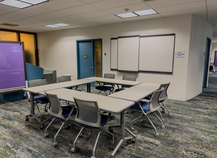 Open area with four tables arranged in a square, eight chairs, three whiteboards and a standing dry erase board