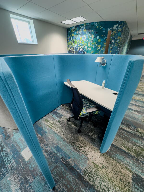 Individual curved fabric work pod with desk, chair, and lamp