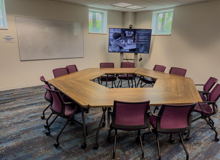 Group tables arranged into a hexagon with 12 chairs, a wall-mounted whiteboard and a screen.