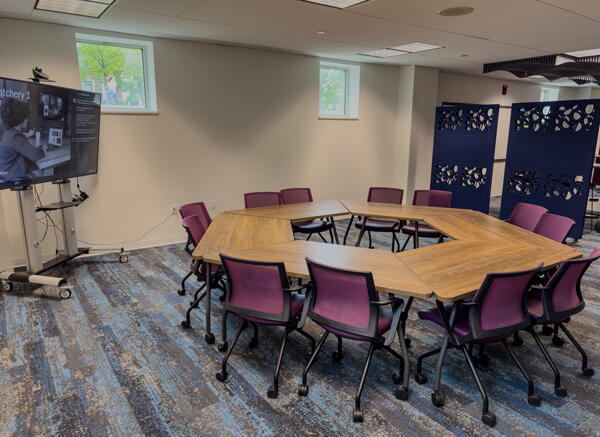 Group tables arranged into a hexagon with 12 chairs, a wall-mounted whiteboard and a screen.
