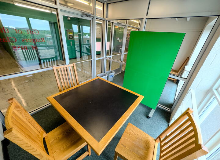 Group study room with square table, four chairs, a rolling green board, and a large window