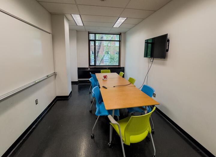 Interior of group study room with long conference table and chairs, wall-mounted display and whiteboard, and a large window