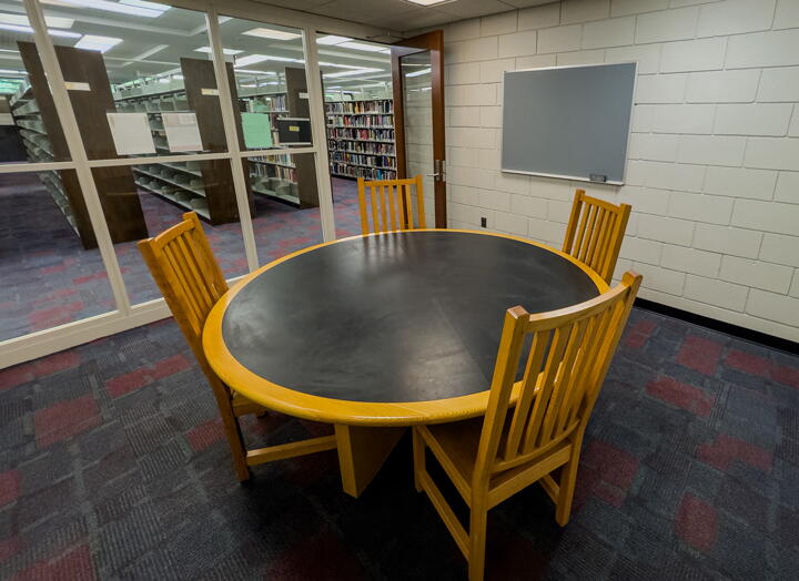 Interior of group study room with small round group table and four chairs, wall-mounted chalkboard, and glass walls