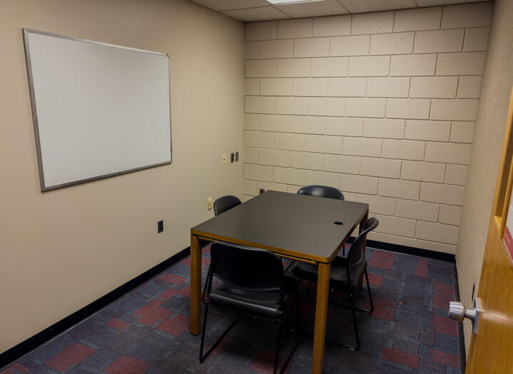 Small group study room with table with four chairs and a wall-mounted whiteboard