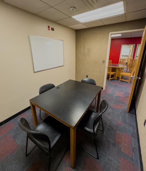 Small group study room with table with four chairs and a wall-mounted whiteboard