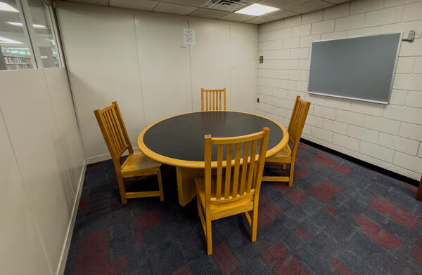 Interior of group study room with small round table with four chairs and a wall-mounted chalkboard