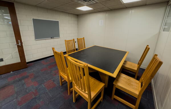 Group study room with square table with six chairs and a wall-mounted chalkboard