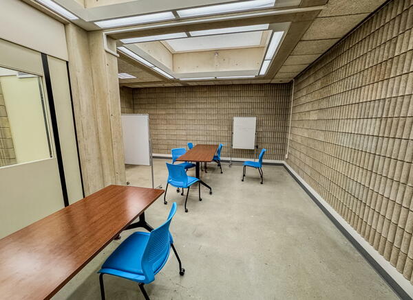 Large L-shaped room with two tables, multiple blue chairs, and two freestanding whiteboards