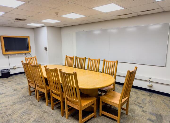 Interior of group study room with a large table, chairs, a video display, and a whiteboard wall