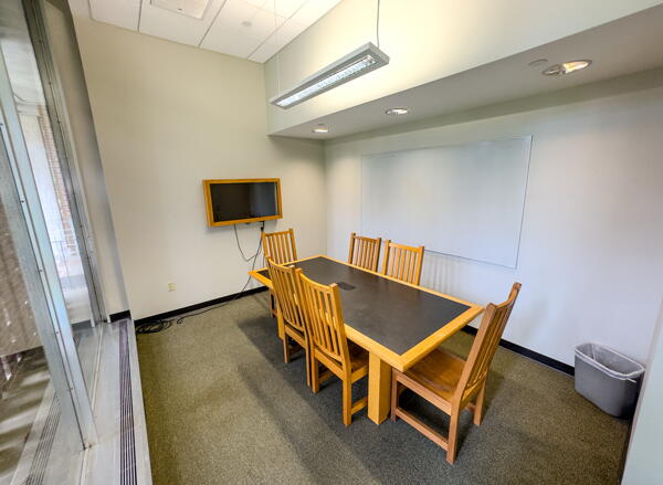 Interior of group study room with a large table, chairs, a video display, and a whiteboard wall