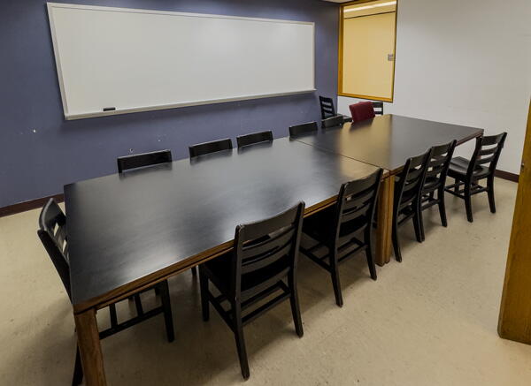Interior of group study room with a large table, 12 chairs, and a whiteboard wall