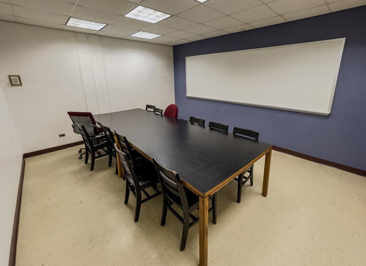 Interior of group study room with a large table, 10 chairs, and a whiteboard wall