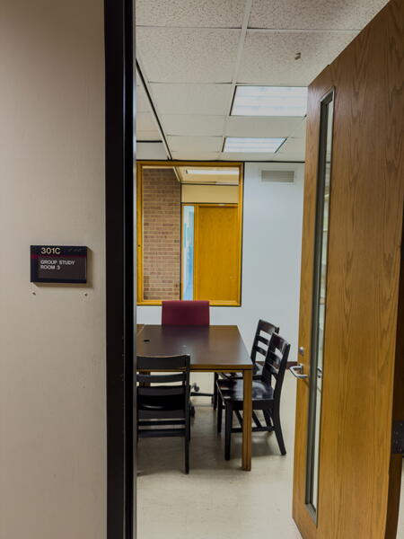 View through open door into group study room with table and chairs