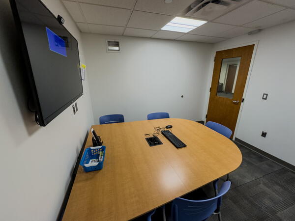 Interior of group study room with a large table, chairs, a wall-mounted display, and a whiteboard wall