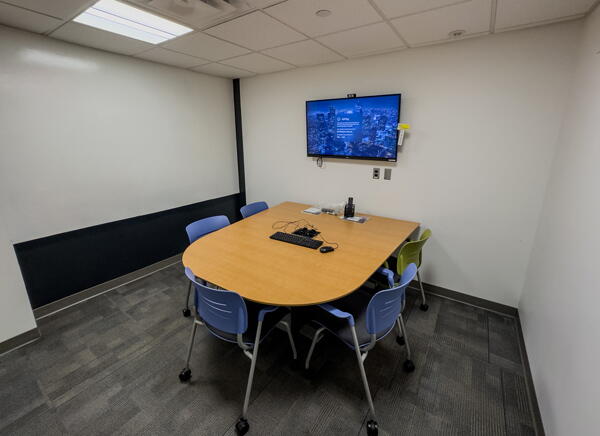 Interior of group study room with a large table, chairs, a wall-mounted display, and a whiteboard wall