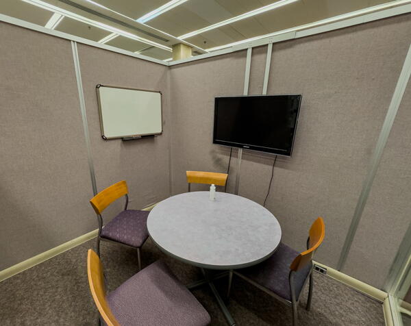 Small group study room with table with four chairs and a wall-mounted whiteboard and display