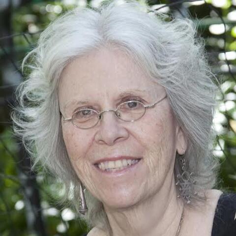 Headshot of a woman with white hair, at about shoulder length with thin wire glasses. She is smiling