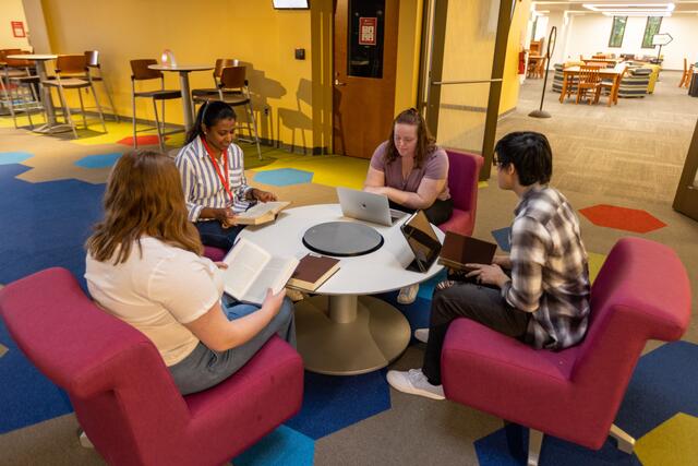 Four students studying in a collaborative work space. they all have different devices to work with