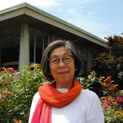 Photo of Kayo in front of the Mabel Smith Douglass library, wearing a white long sleeve top and a pink and orange scarf